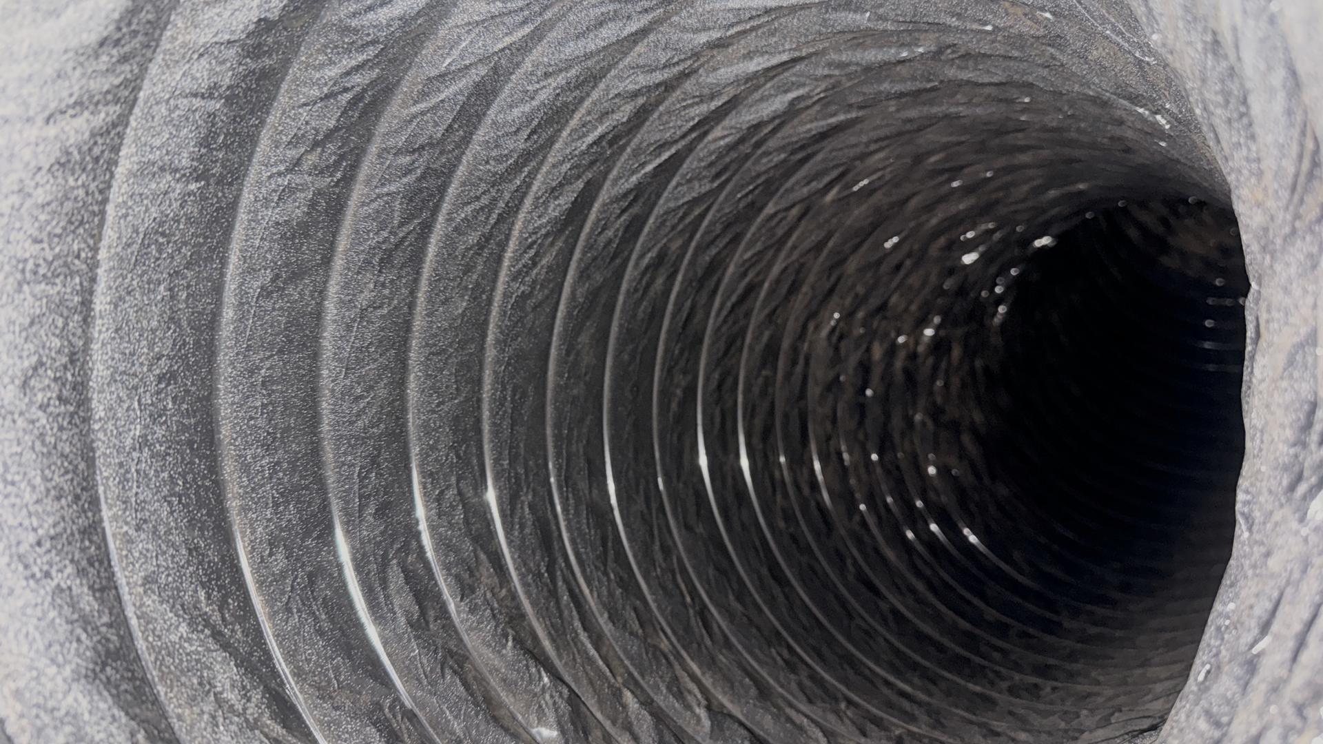 View along the inside of a flexible supply duct, its walls coated in grey dust